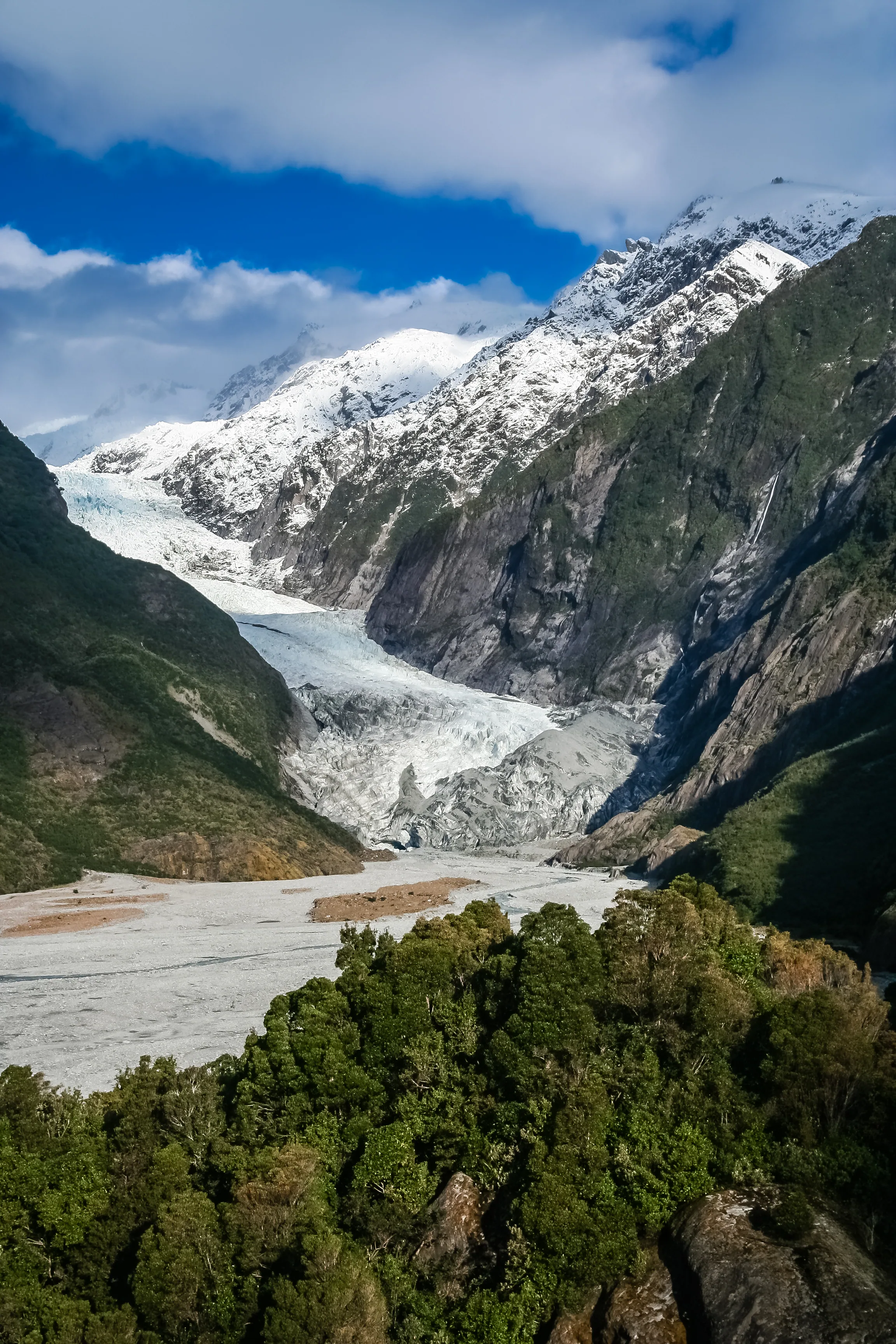 Franz Josef Glacier from the valley floor, ice flowing down between bush-clad mountain walls