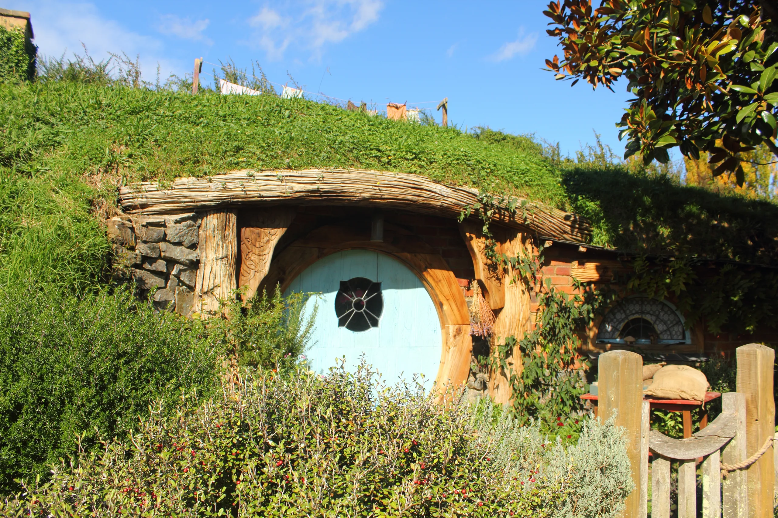 A hobbit house built into a green hillside with a round light-blue door and a small round window