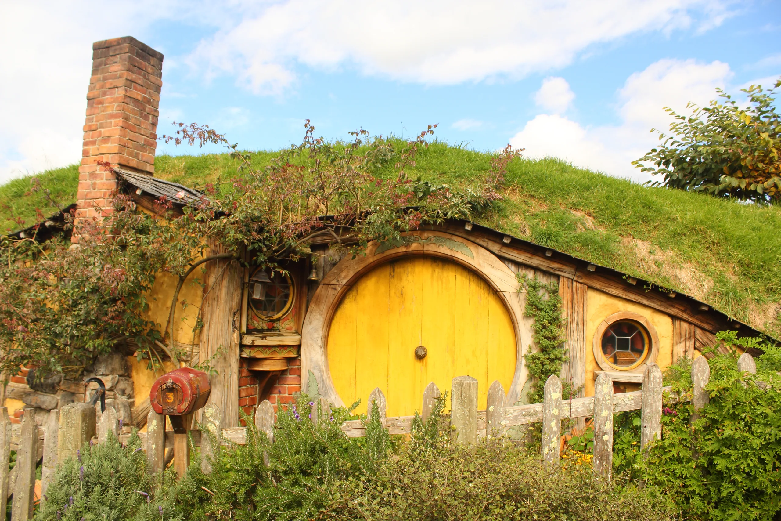 A hobbit hole at the Hobbiton Movie Set with a round green door and garden