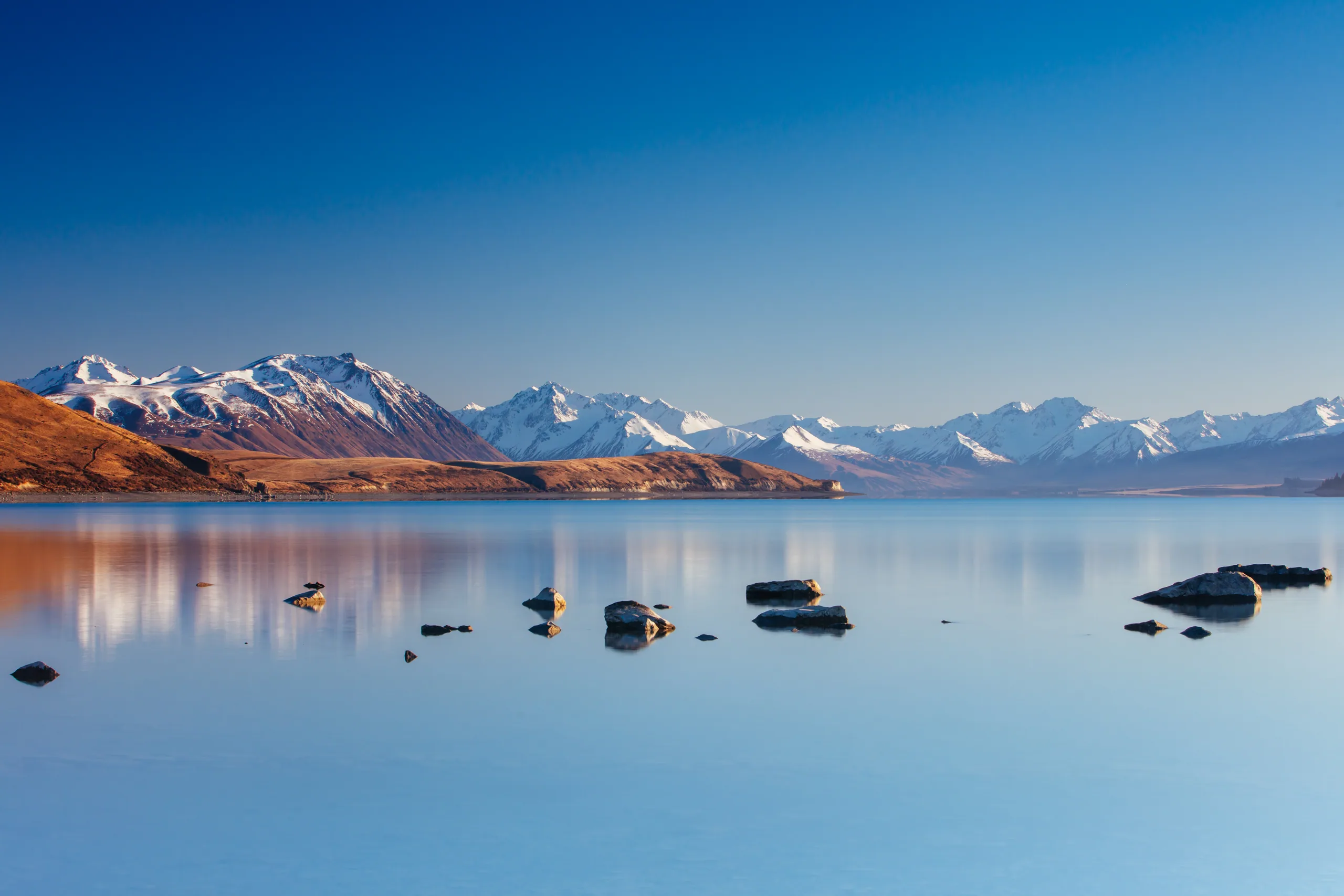 Lake Tekapo at sunset with the turquoise water turning pink and the Southern Alps behind