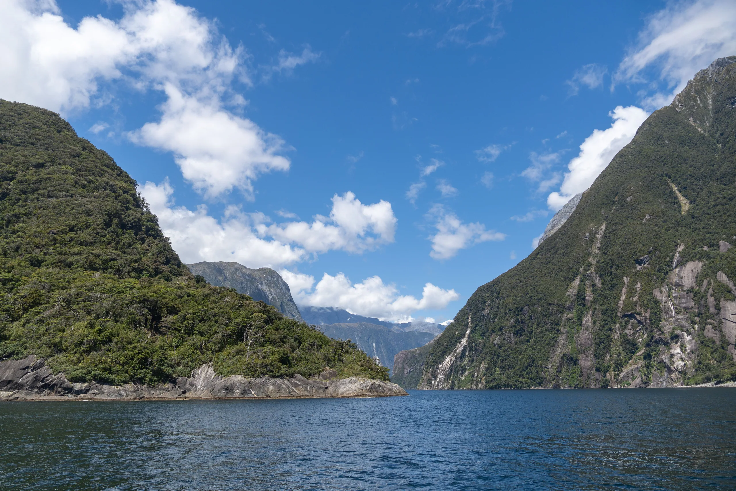 Snow-capped peaks above a dark Fiordland fjord with low cloud and mist