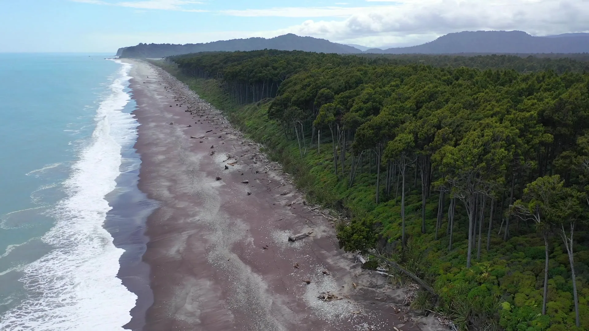 A coastal highway curving along a beach with green hills and a small town in the distance