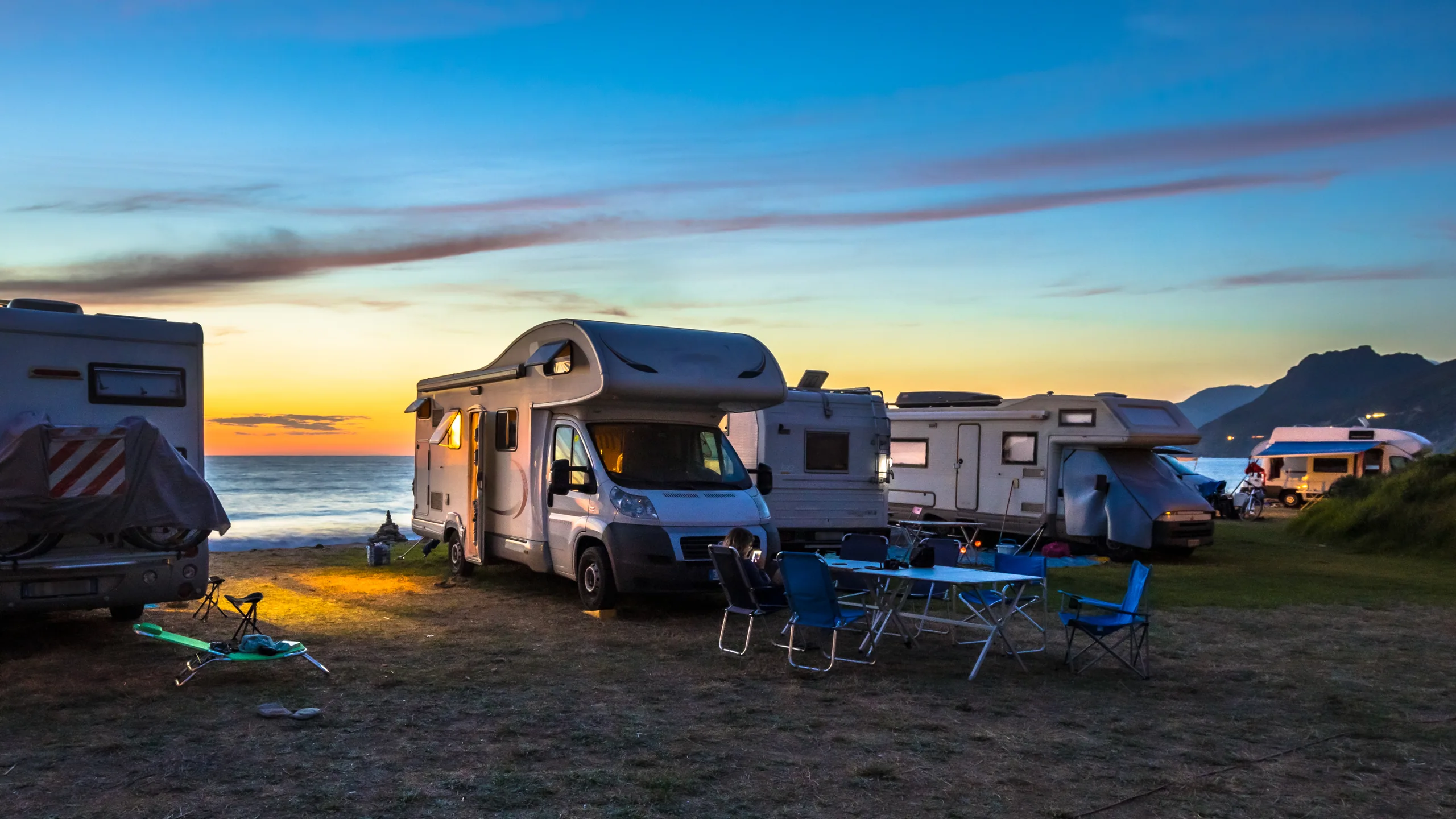 A line of campervans on powered sites at a New Zealand holiday park with mountains in the background