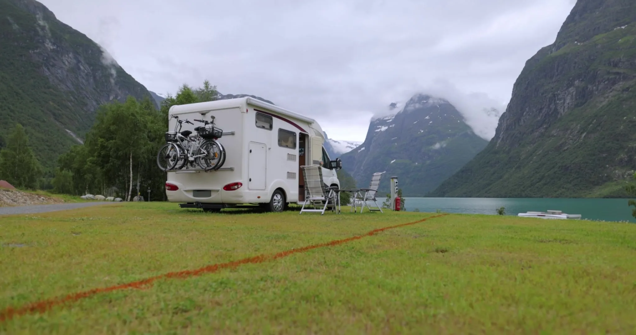 Two travellers cooking outside their campervan beside a lake at sunset