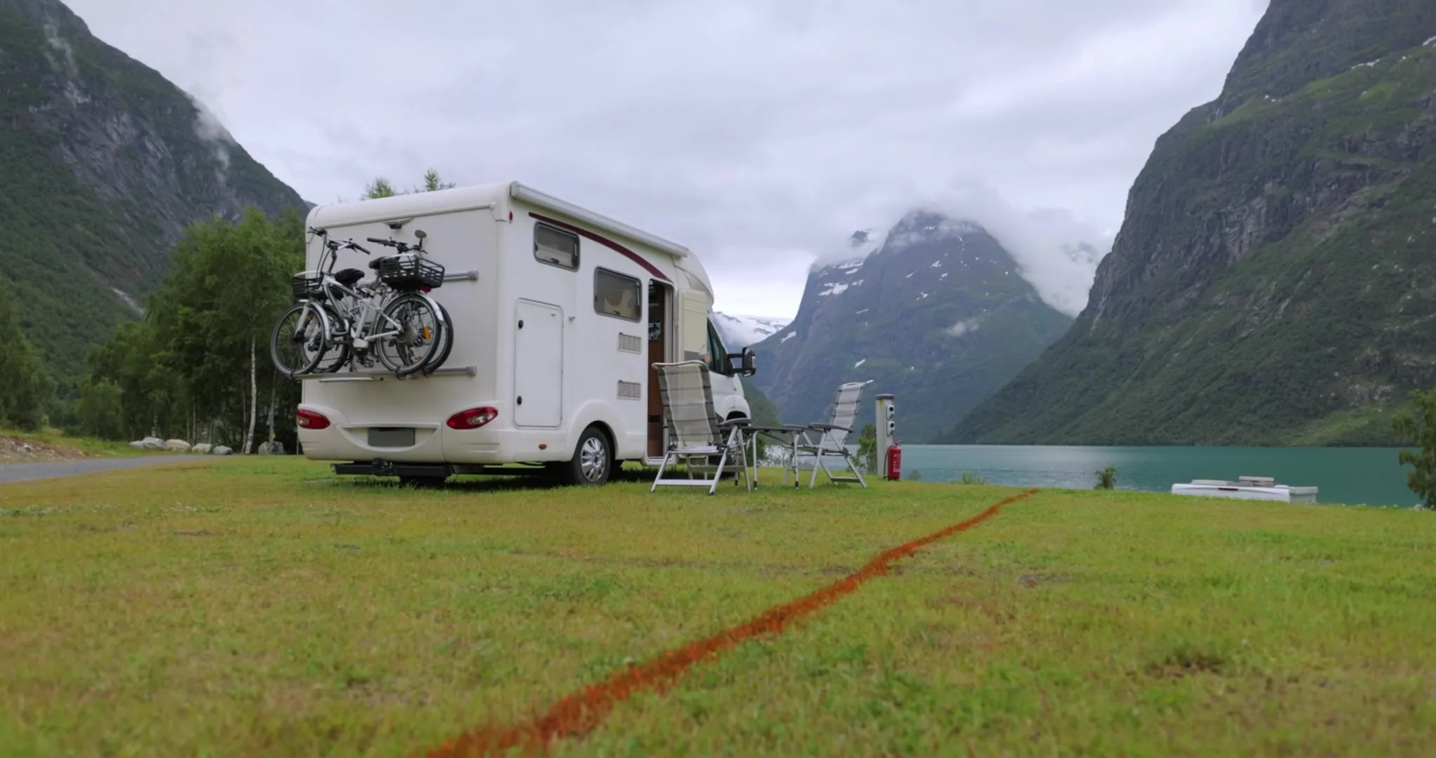 A white campervan parked on a gravel pullout above a glacial lake with snow-capped peaks behind