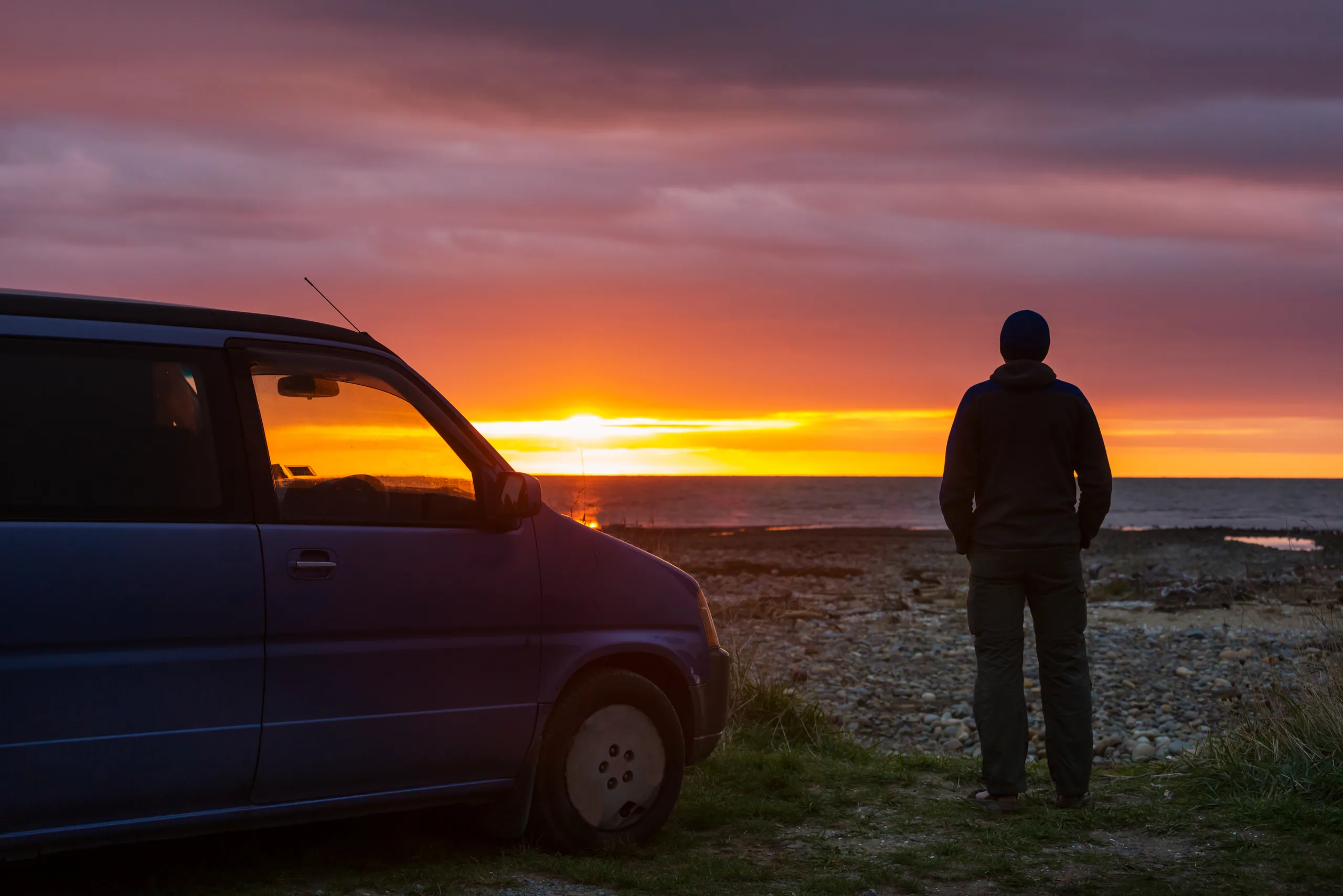 A campervan parked on the ocean shore in summer with surfboard on the roof